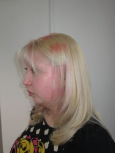 Close-up of bright blonde hair featuring horizontal pink "raccoon stripe" chunky highlights and a creative double-process color finish