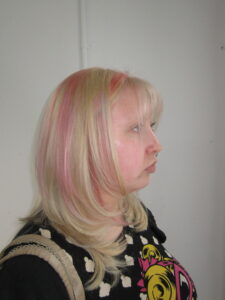 Close-up of bright blonde hair featuring horizontal pink "raccoon stripe" chunky highlights and a creative double-process color finish
