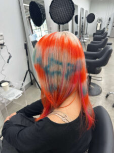 A close-up of a vibrant "Triple Process Creative Colour" on long hair, orange and blue stripe designs performed at Assort Melbourne.