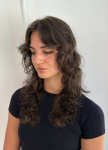 A client at Assort Melbourne salon showcasing frizz-free, voluminous curly hair with soft layers, demonstrating professional curly hair maintenance.