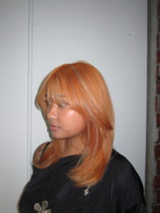 Vibrant electric orange hair with blonde highlights and a fresh haircut, styled with high shine.