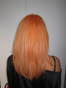 Vibrant electric orange hair with blonde highlights and a fresh haircut, styled with high shine.