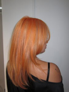 Vibrant electric orange hair with blonde highlights and a fresh haircut, styled with high shine.