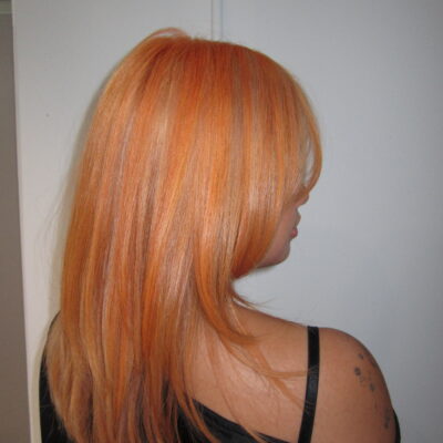 Vibrant electric orange hair with blonde highlights and a fresh haircut, styled with high shine.