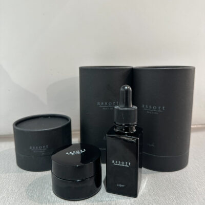 A close-up of Assort Brand Light Oil, Rich Oil, and Styling Balm bottles on a minimalist wooden counter at Assort Melbourne.