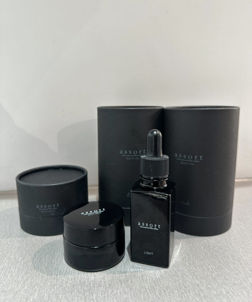 A close-up of Assort Brand Light Oil, Rich Oil, and Styling Balm bottles on a minimalist wooden counter at Assort Melbourne.