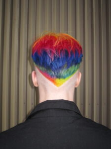 Vivid rainbow hair transformation at Assort Melbourne featuring saturated layers of purple, green, and orange with a high-shine "glass hair" finish.